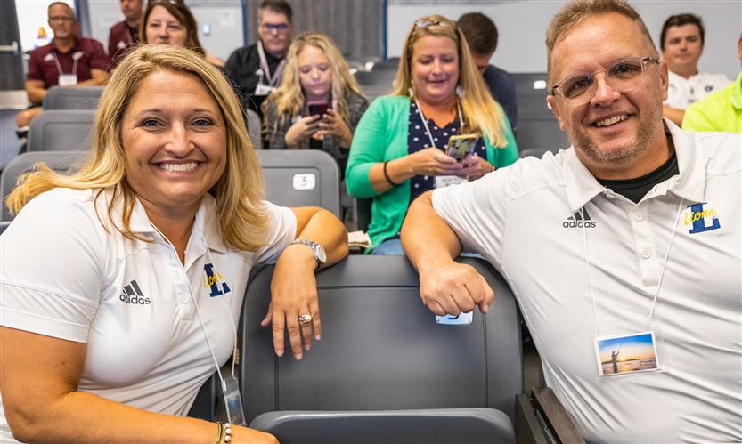 Two administrators sit in auditorium seats and lean together
